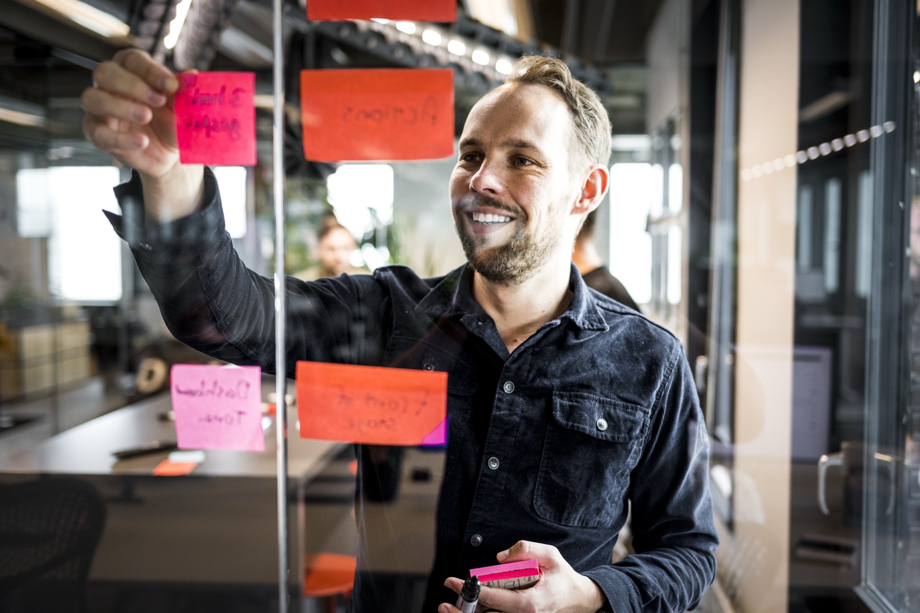 Iemand plakt een post-it op een glazen wand vol memos